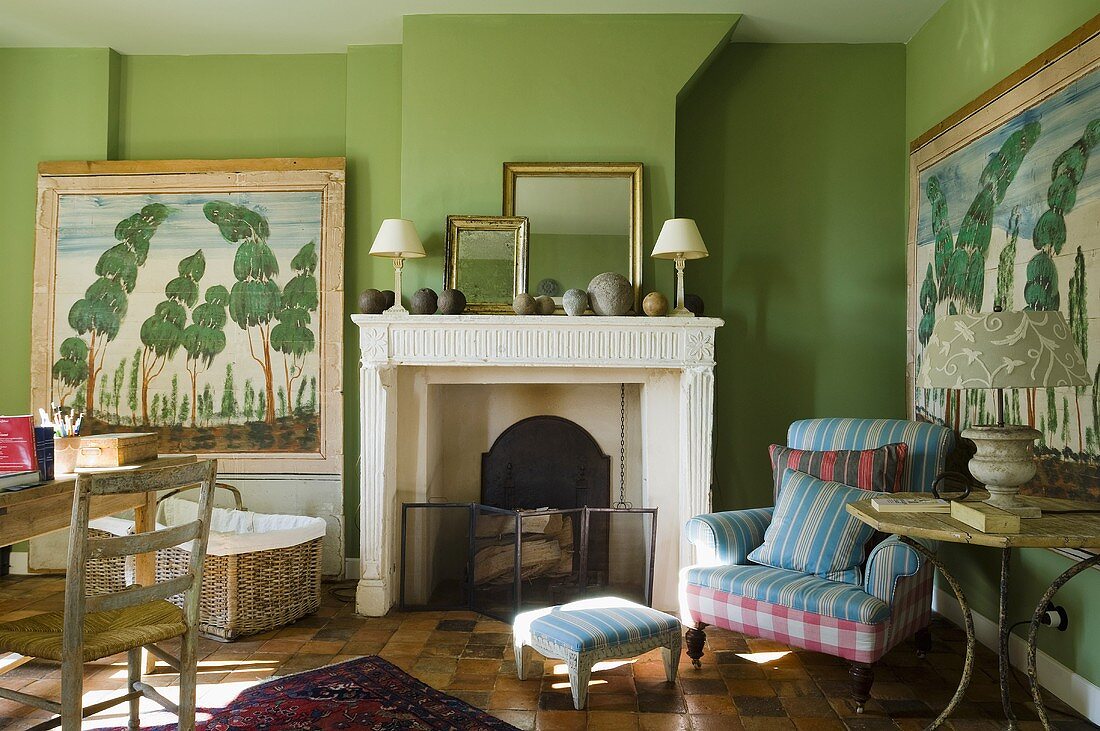 A cosy fireplace room with an upholstered armchair and footstool against a green wall
