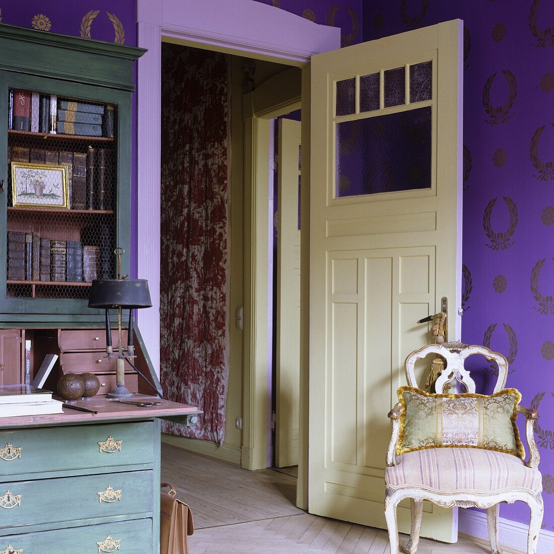 An antique Rococo-style chair in front of an open door with a view into a hallway