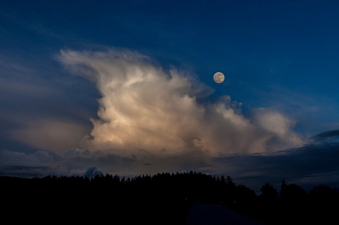 Storm cloud over forest at full moon, Chiemgau, Bavaria, Germany