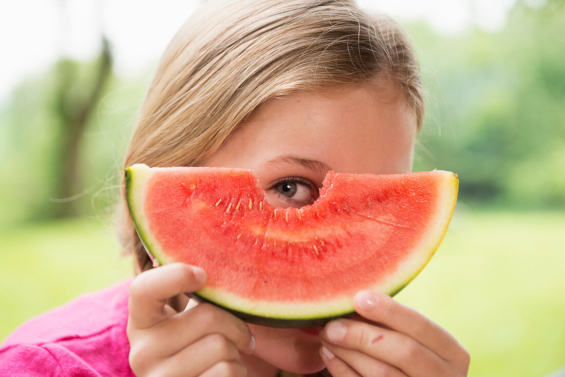 Close up portrait of girl peering through watermelon slice