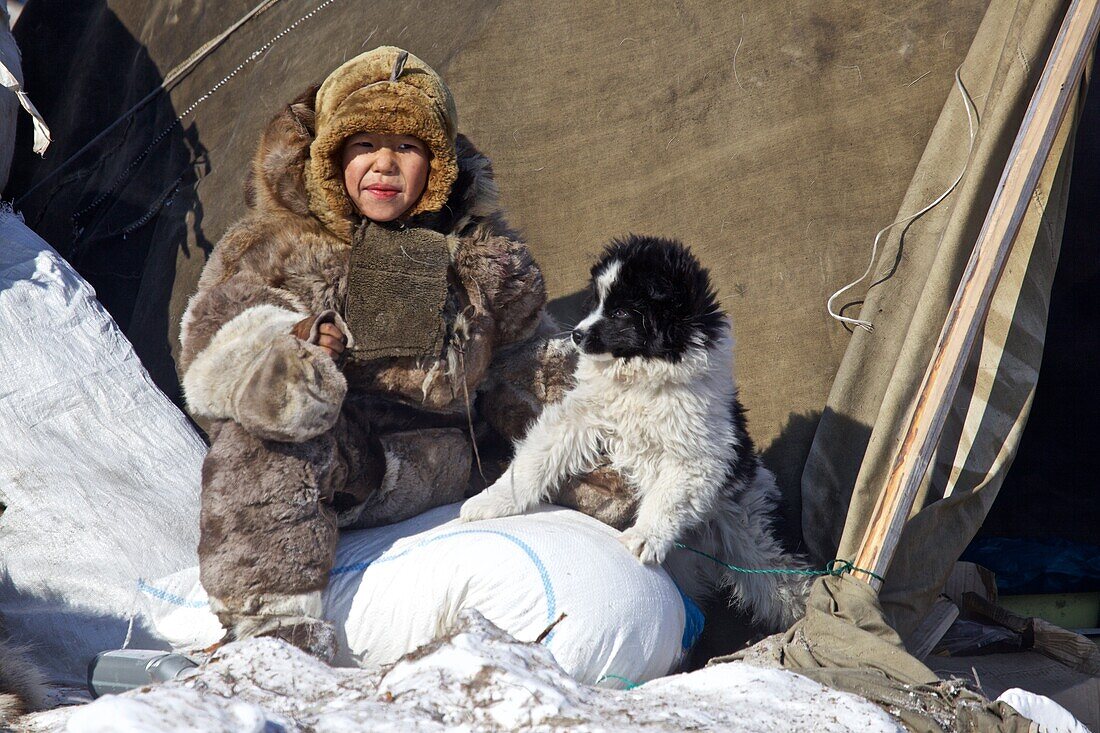 mit Rentierfellen bekleidetes Nomaden-Kind mit jungem Hund, Tschukotka (Autonomer Kreis der Tschuktschen), Sibirien, Russland