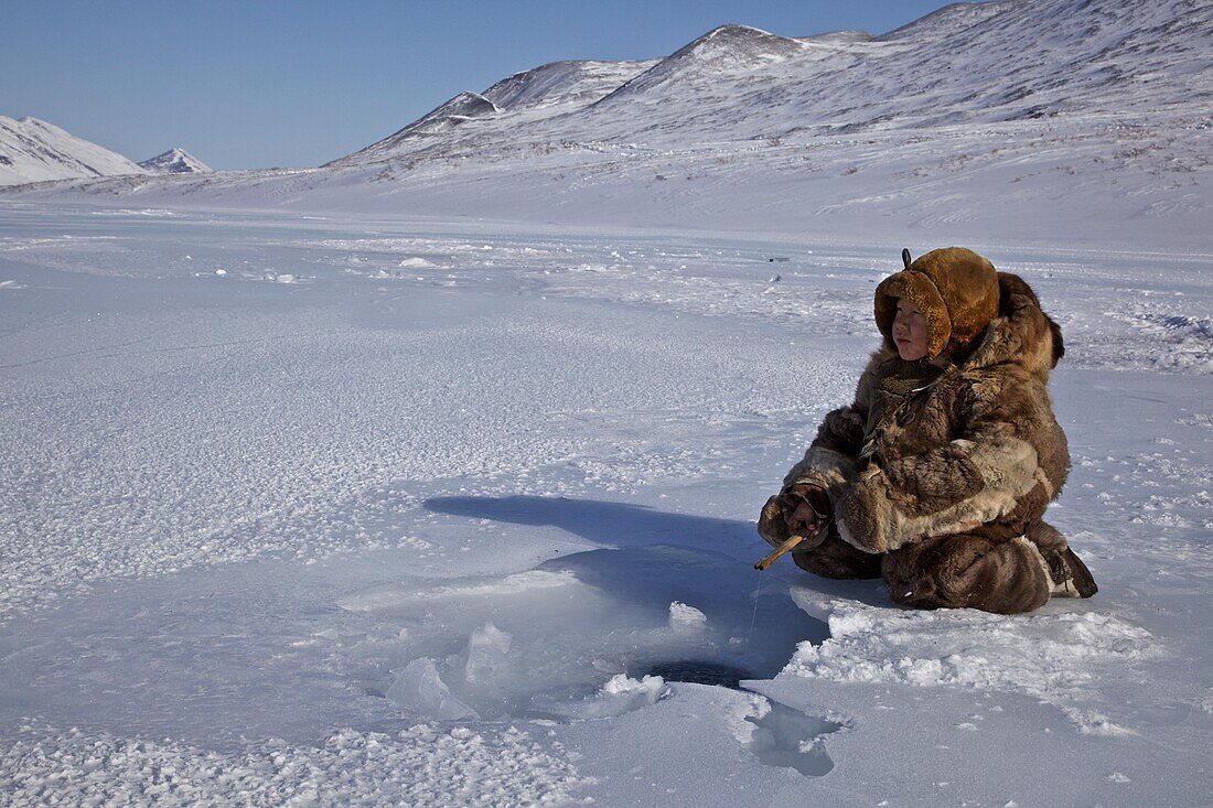 Reindeer nomad boy dressed in reindeer skins ice fishing, Chukotka Autonomous Okrug, Siberia, Russia