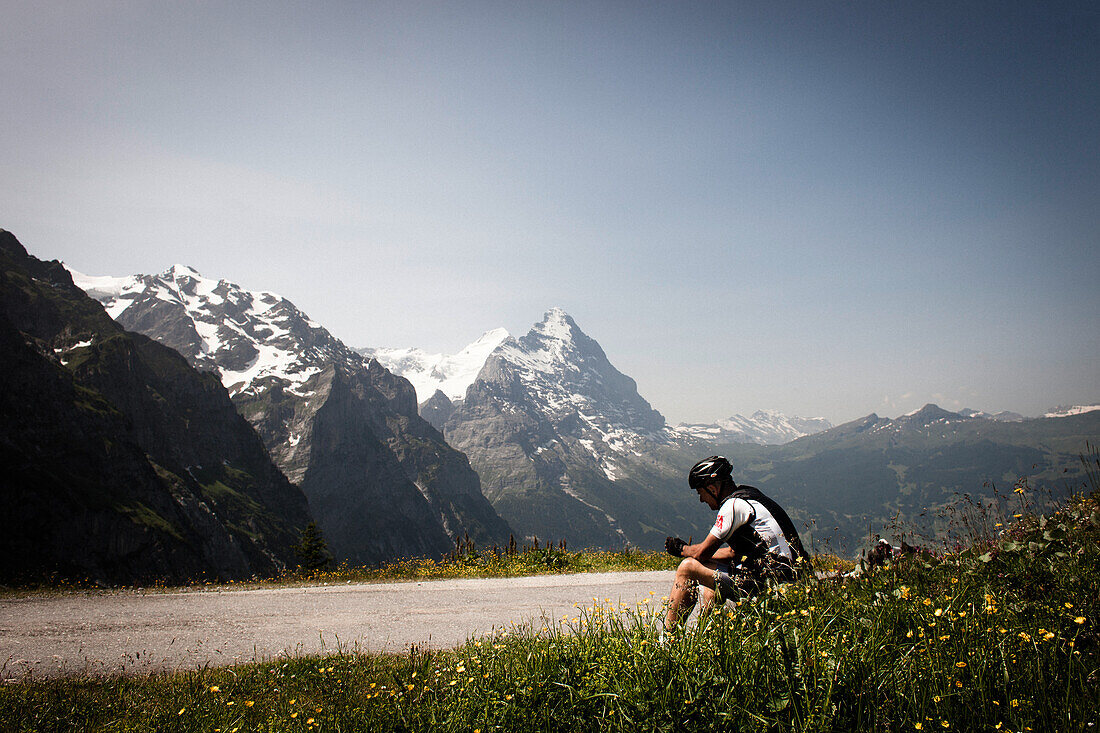 Cyclist taking a rest on a mountain pass, Eiger and Moench in the background, descent from Grosse Scheidegg to Grindelwald, Bernese Oberland, Switzerland