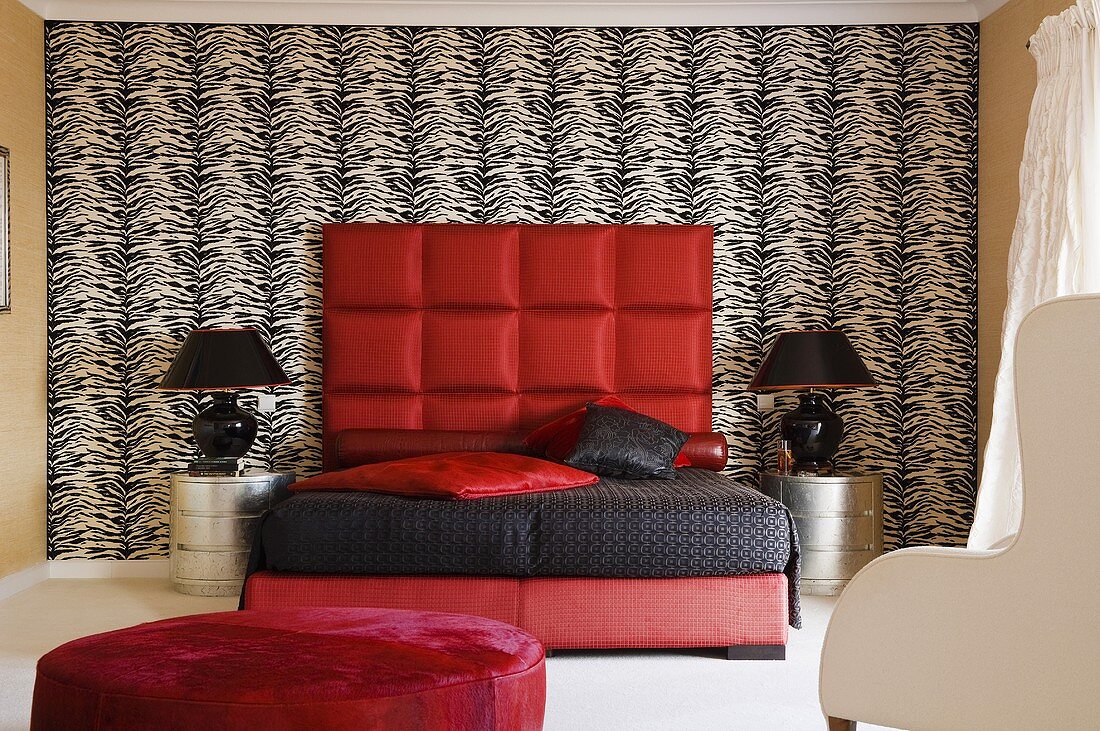 A funky bedroom - a red bed with a black cover and an upholstered headboard against a black and white wall