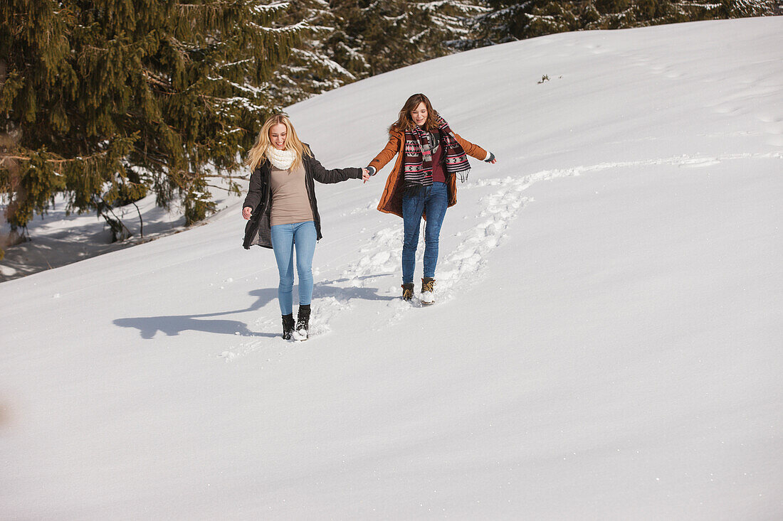 Two young women walking hand in hand in snow, Spitzingsee, Upper Bavaria, Germany