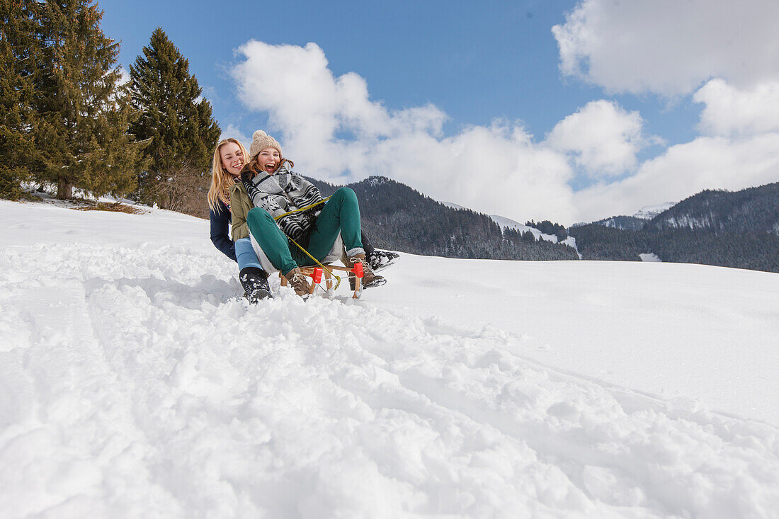 Two young women downhill sledding, Spitzingsee, Upper Bavaria, Germany