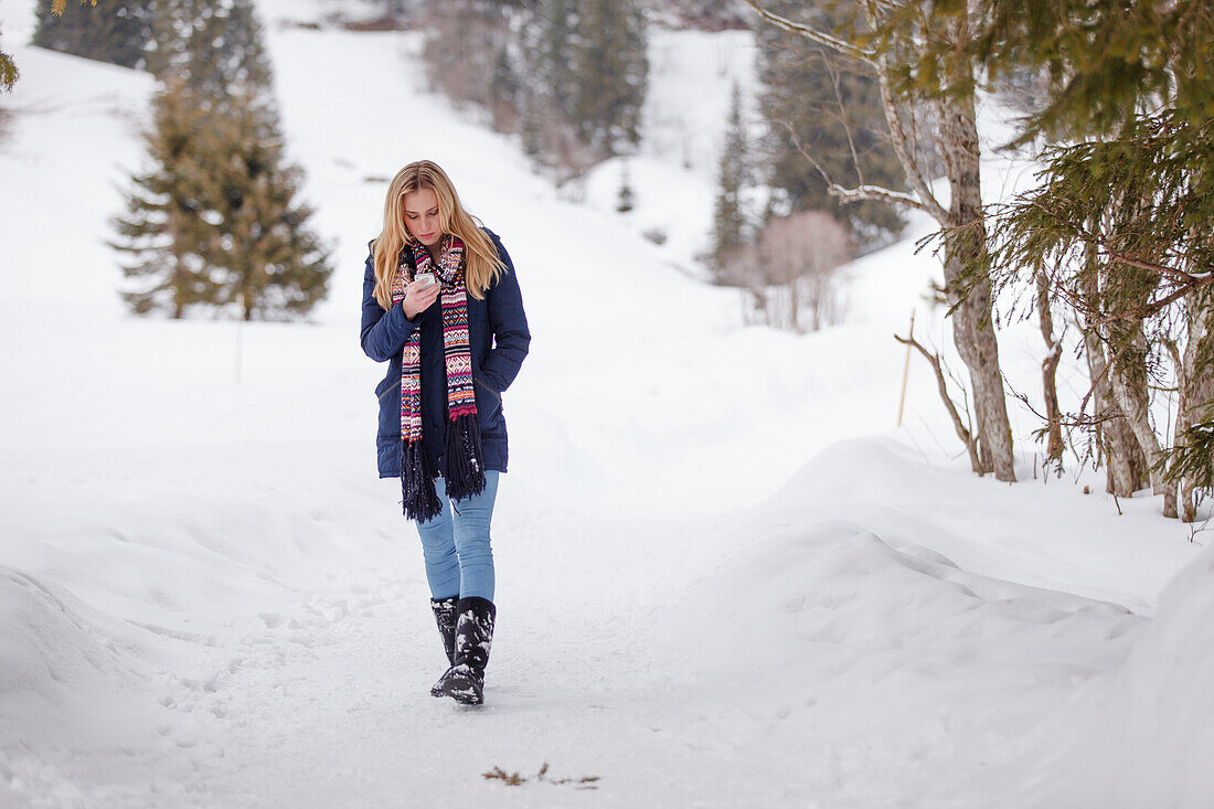 Junge Frau mit einem Handy läuft durch den Schnee, Spitzingsee, Oberbayern, Bayern, Deutschland