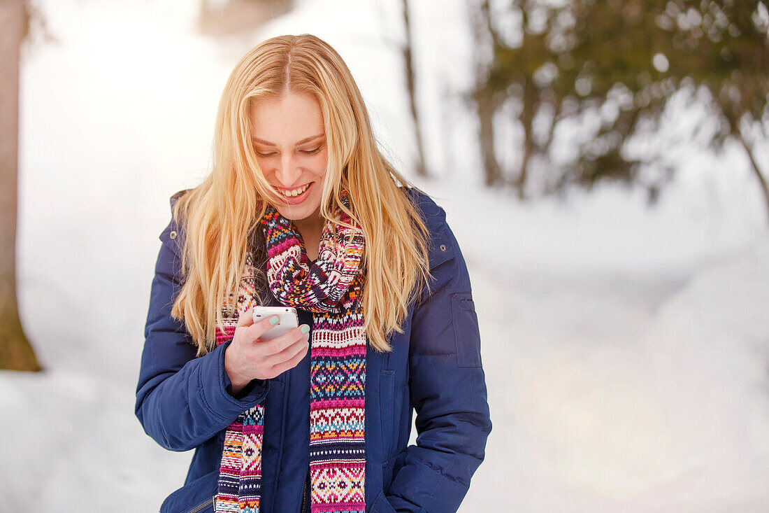 Junge Frau hält ein Smartphone in der Hand und lächelt, Spitzingsee, Oberbayern, Bayern, Deutschland
