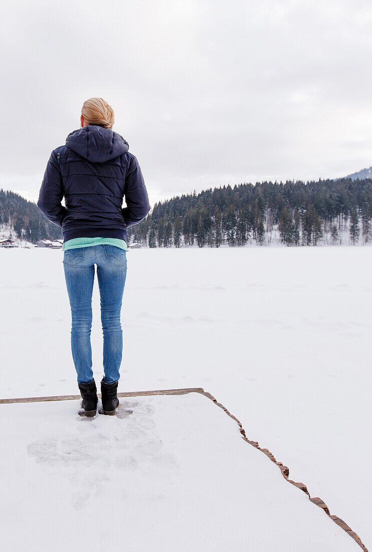 Junge Frau auf einem Steg am schneebedeckten Spitzingsee, Bayern, Deutschland