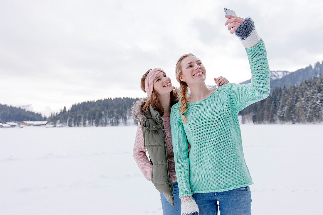 Two young women photographing themselves, Spitzingsee, Upper Bavaria, Germany
