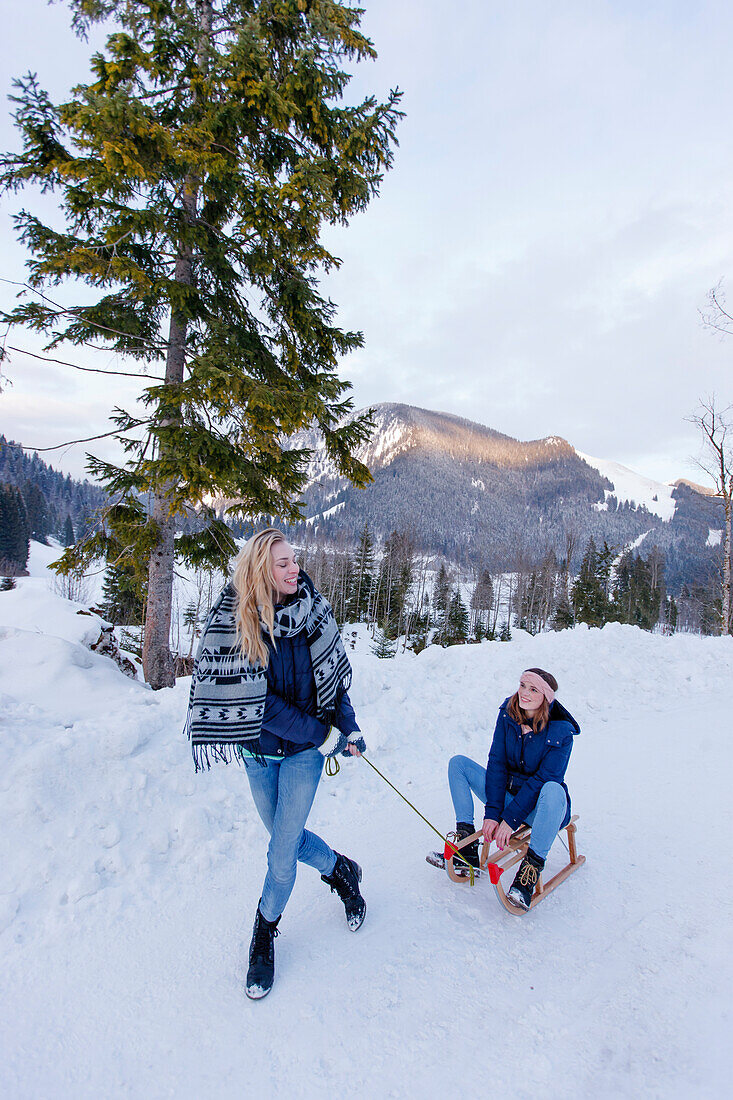 Young woman pulling a sled with woman, Spitzingsee, Upper Bavaria, Germany