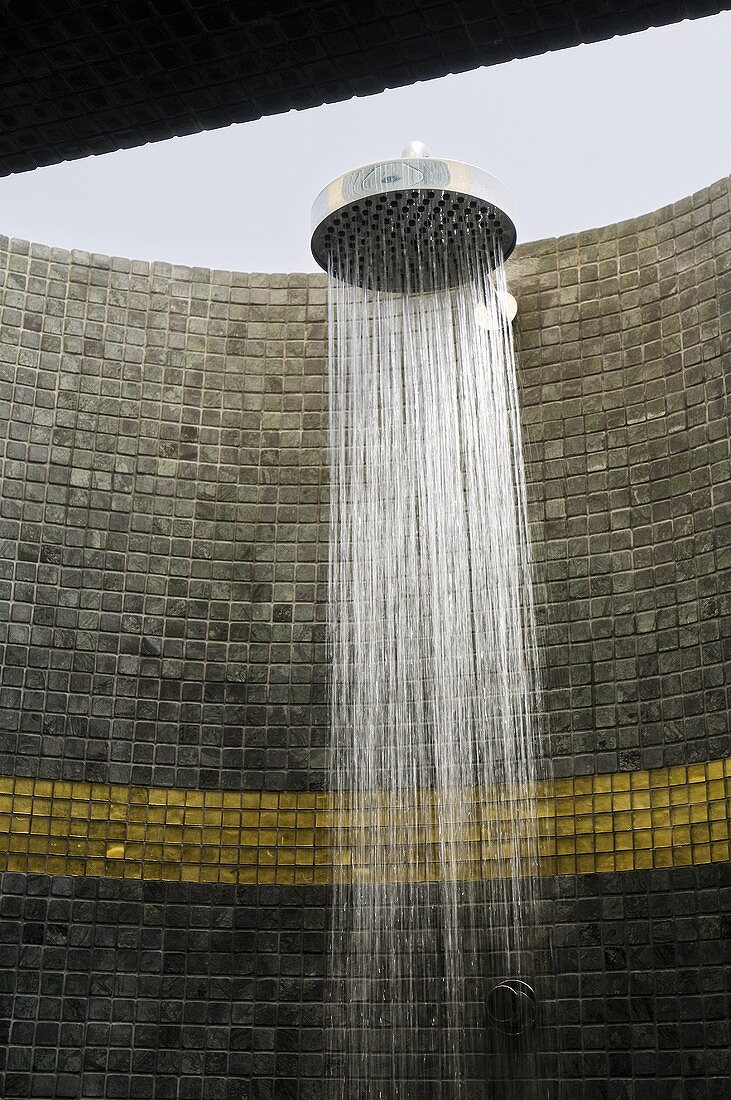 Mosaic tiles on the wall of a shower with a running shower head