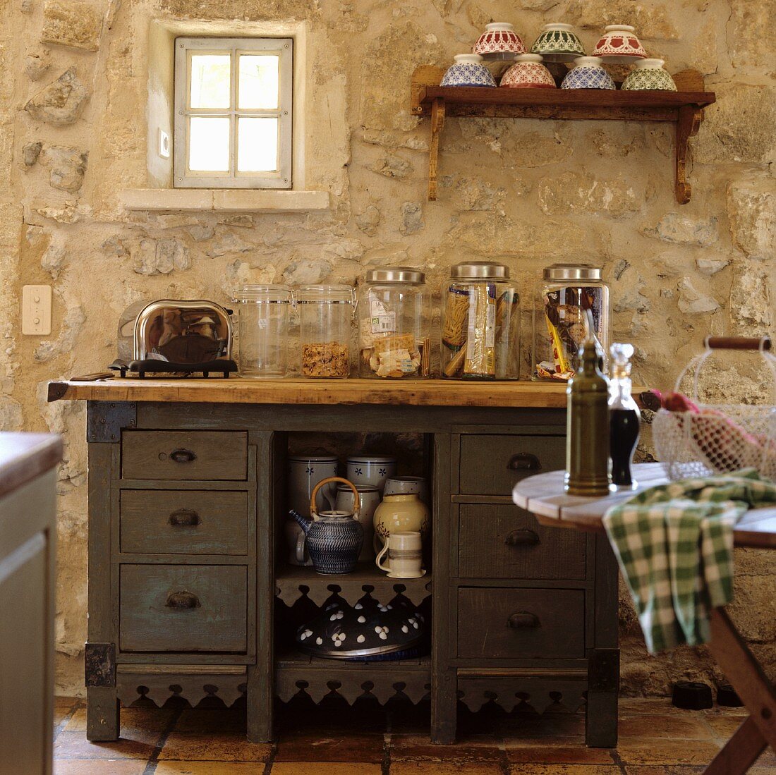 Storage jars on an old kitchen drawer unit in front of a rustic, natural stone wall