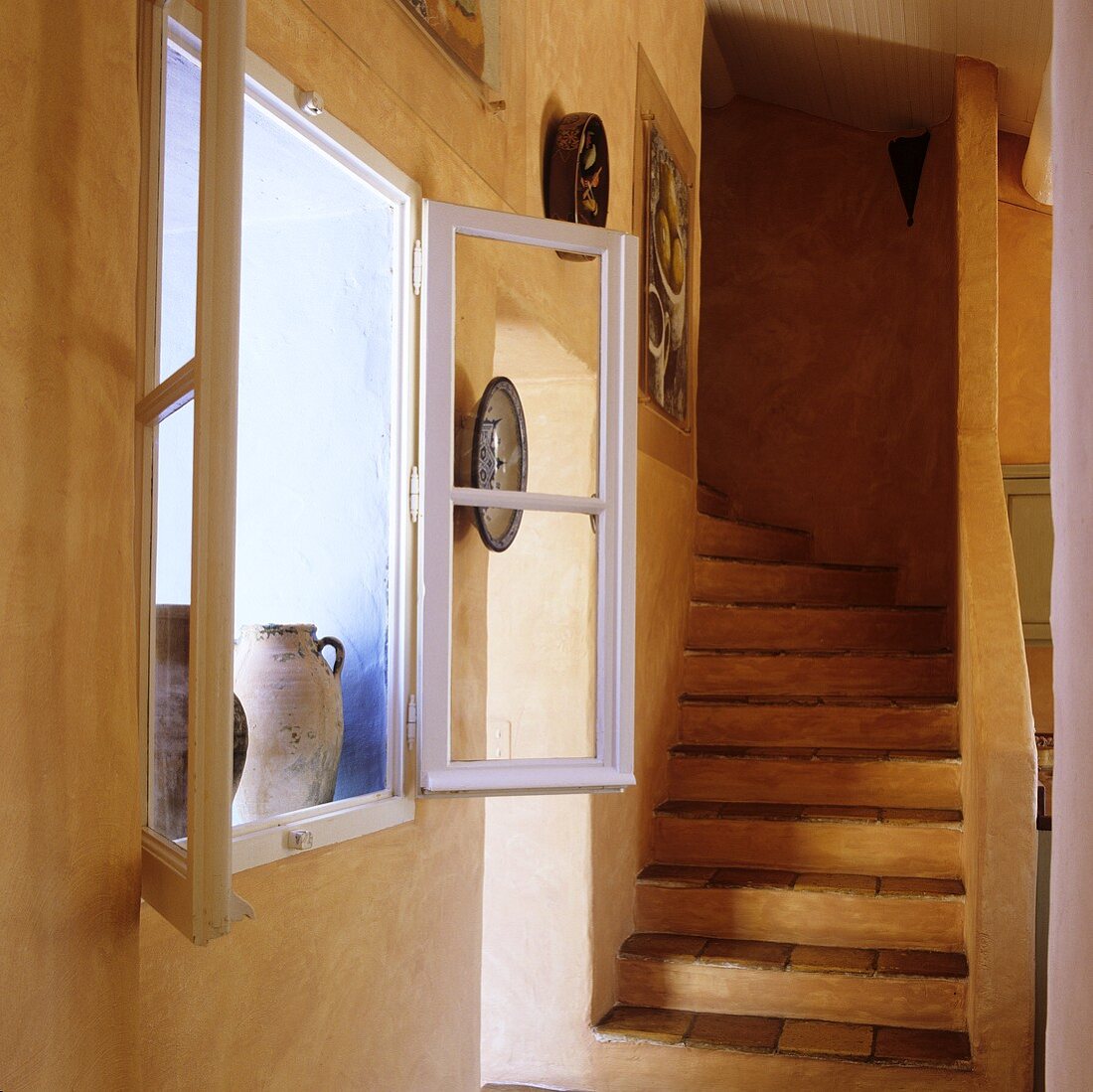 An open window set into an apricot wall and a flight of stairs in a rustic country house