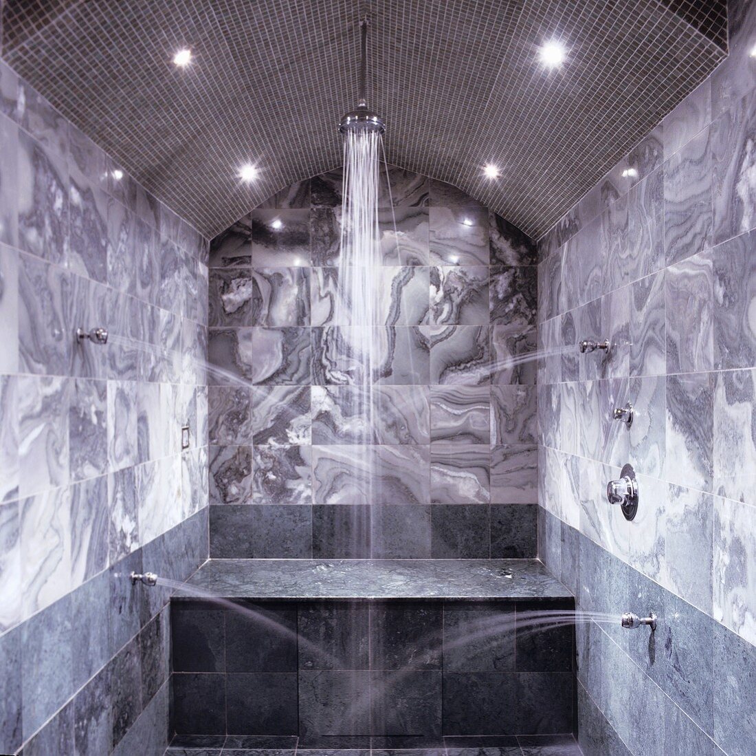 A marble bathroom oasis - water pouring out of side spouts with a shower head between spotlights