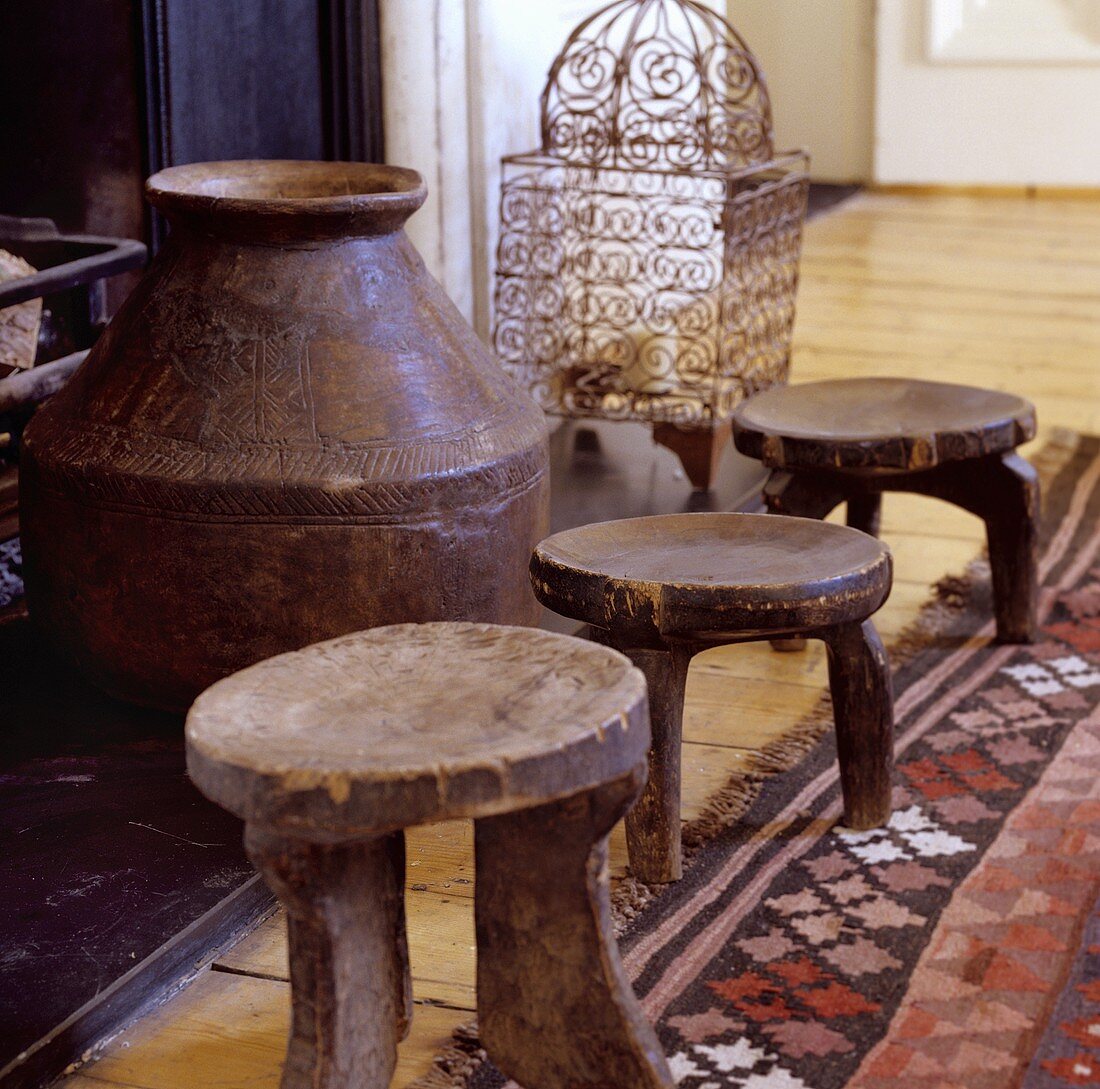 Three rustic wooden stools in front of an amphora