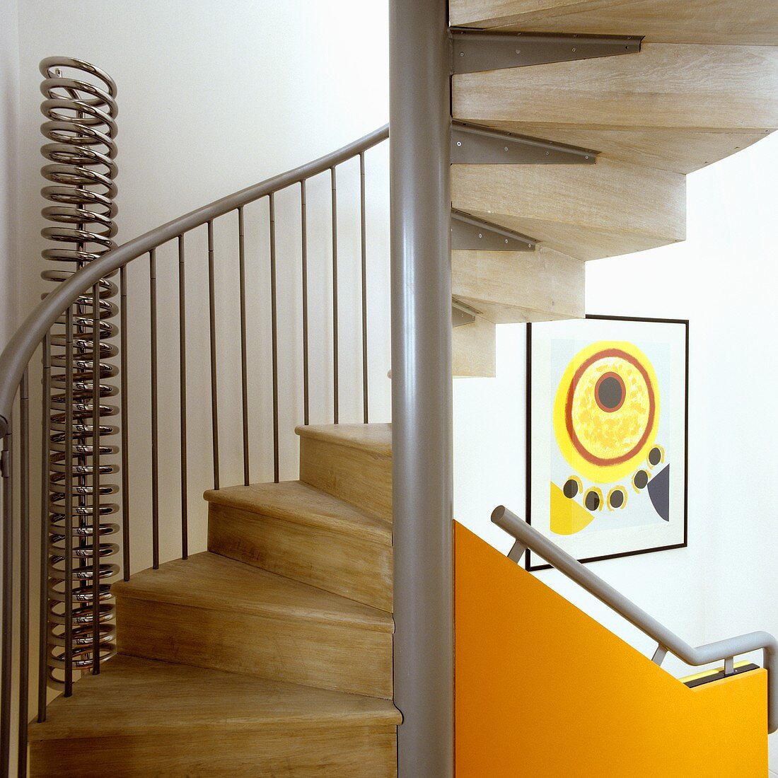 A spiral staircase with a metal frame and wooden stairs and a handrail on an orange-colored panel