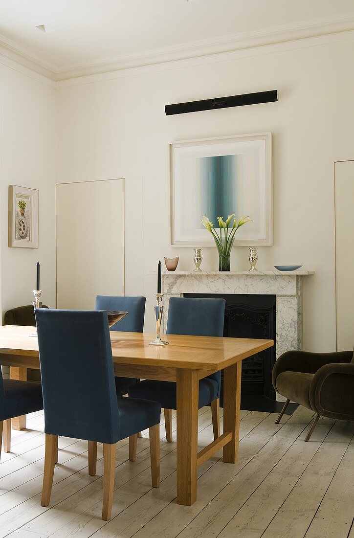 A room with rustic floor boards and a dining table with upholstered chairs in front of a fireplace