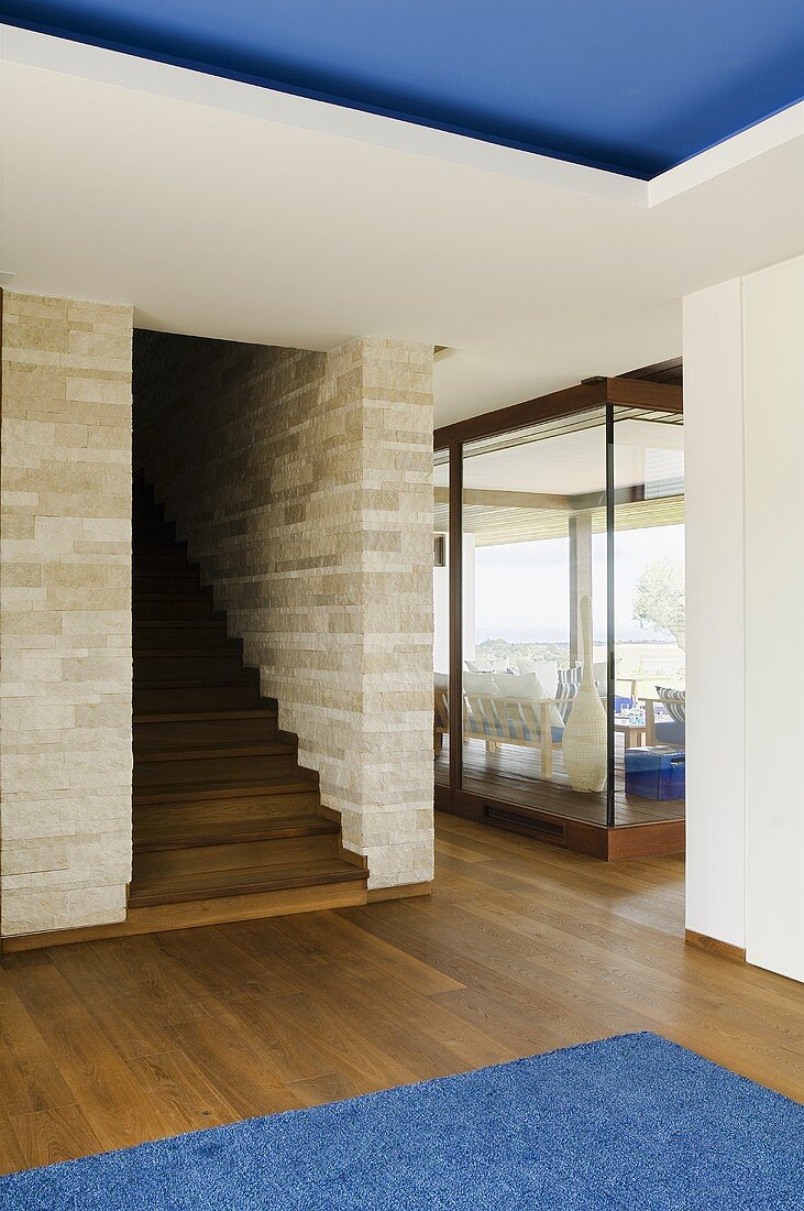Vorraum mit Nussholzboden und Holztreppenaufgang in Natursteinwand mit Blick auf Glasfassade