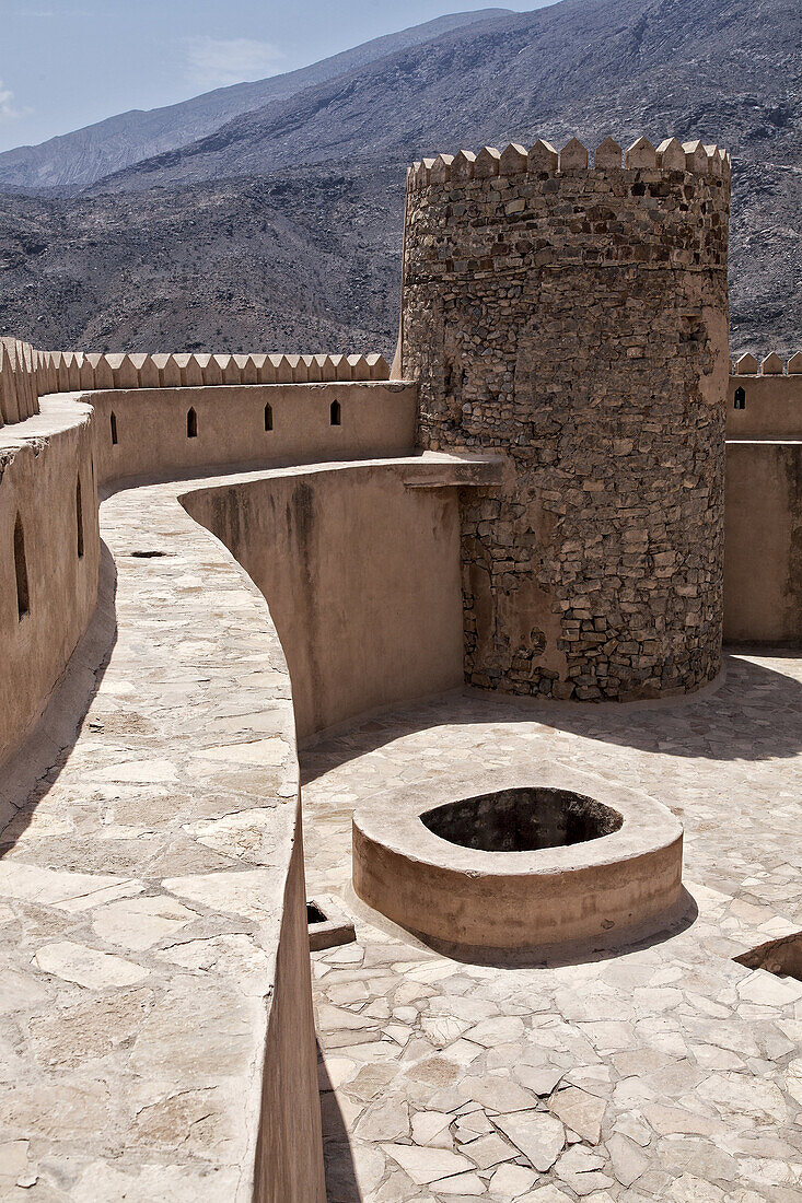 View of the battlements, tower, well and courtyard of Rustaq Fort with the Hajar Mountains in the background, Rustaq, Al Batinah South Governorate, Oman.