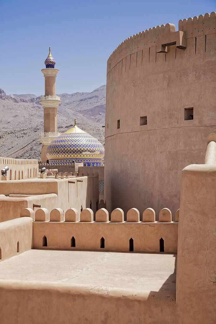 General view of Nizwa Fort with the minaret of the As Sultan Qaboos Mosque in the background, Al Jinah, Nizwa, Ad Dakhiliyah Governorate, Oman.