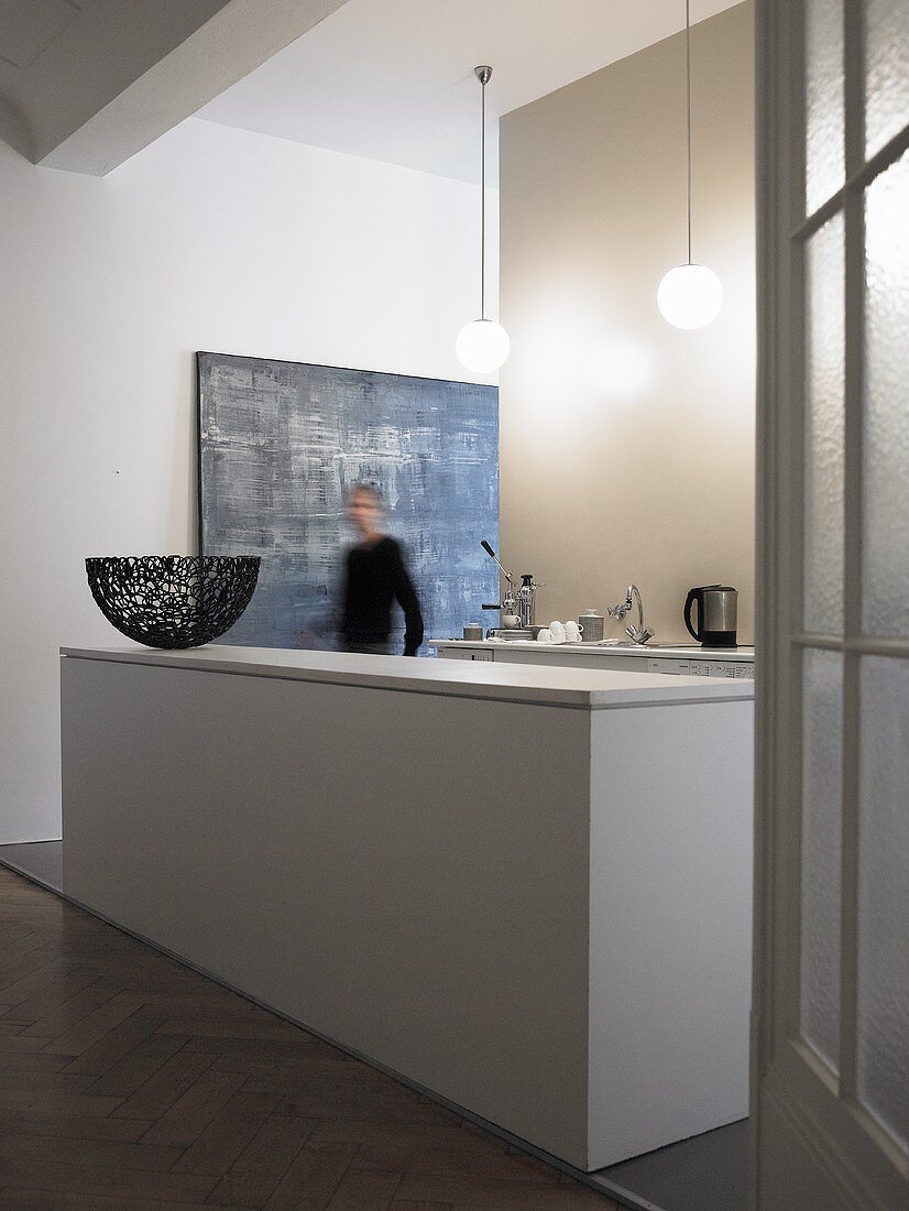 An open-plan kitchen in a minimalistic anteroom - a white monolithic kitchen counter and a man in the hallway