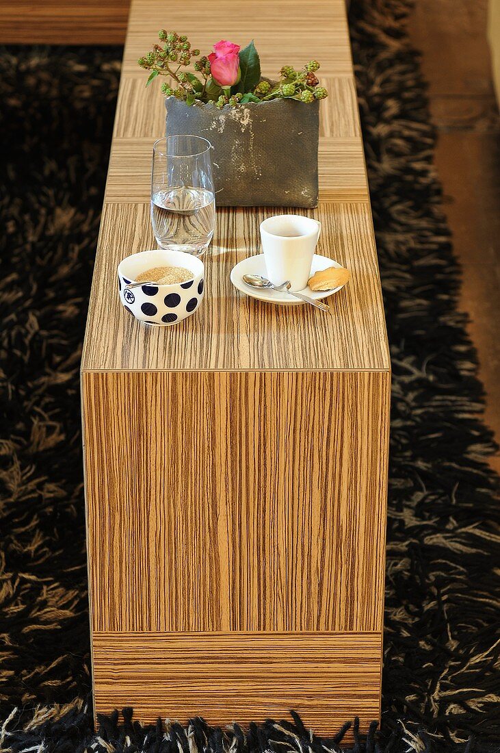 Kaffeegedeck und Blumendeko auf furniertem Holztisch