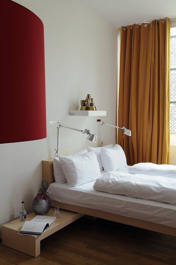 A designer wooden bed with reading lamps and yellow curtains at the window