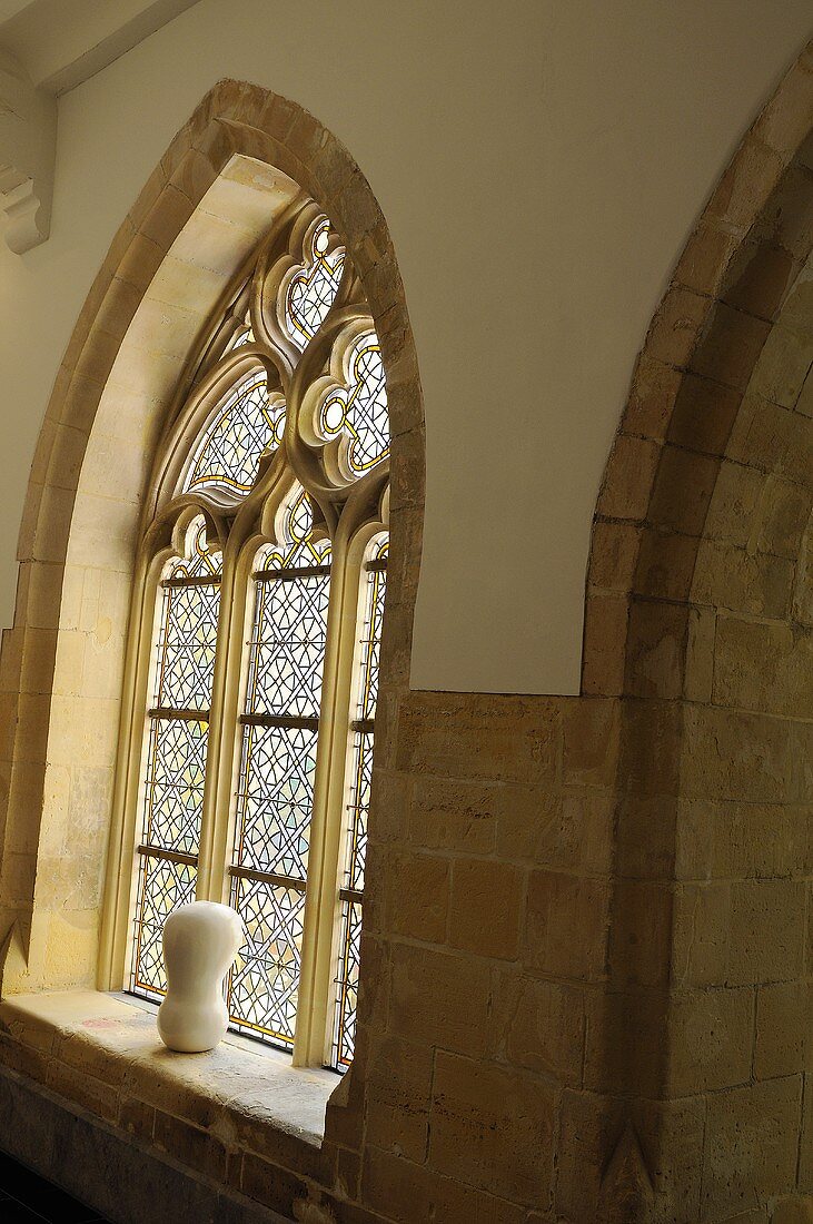 A Gothic pointed arch with stain glass and a sculpture on the window sill