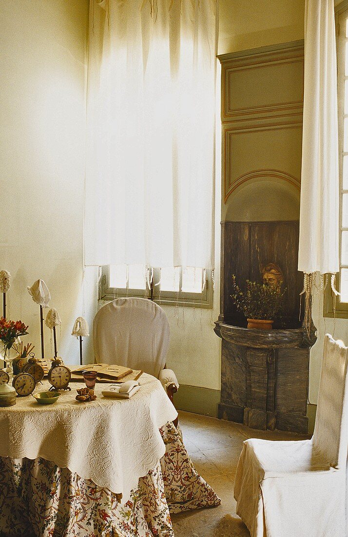 A corner of a living room with a stone basin in a wall niche next to a window, a table and covered chairs