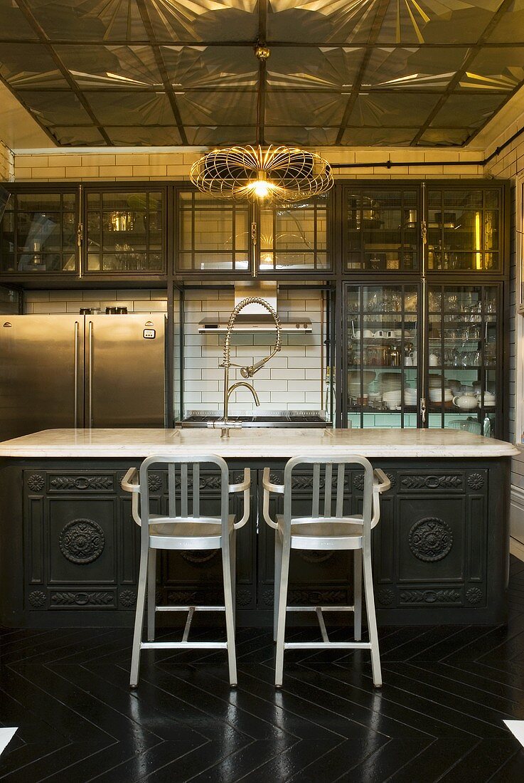 A traditional, open-plan kitchen with metal bar stools and artificial lighting