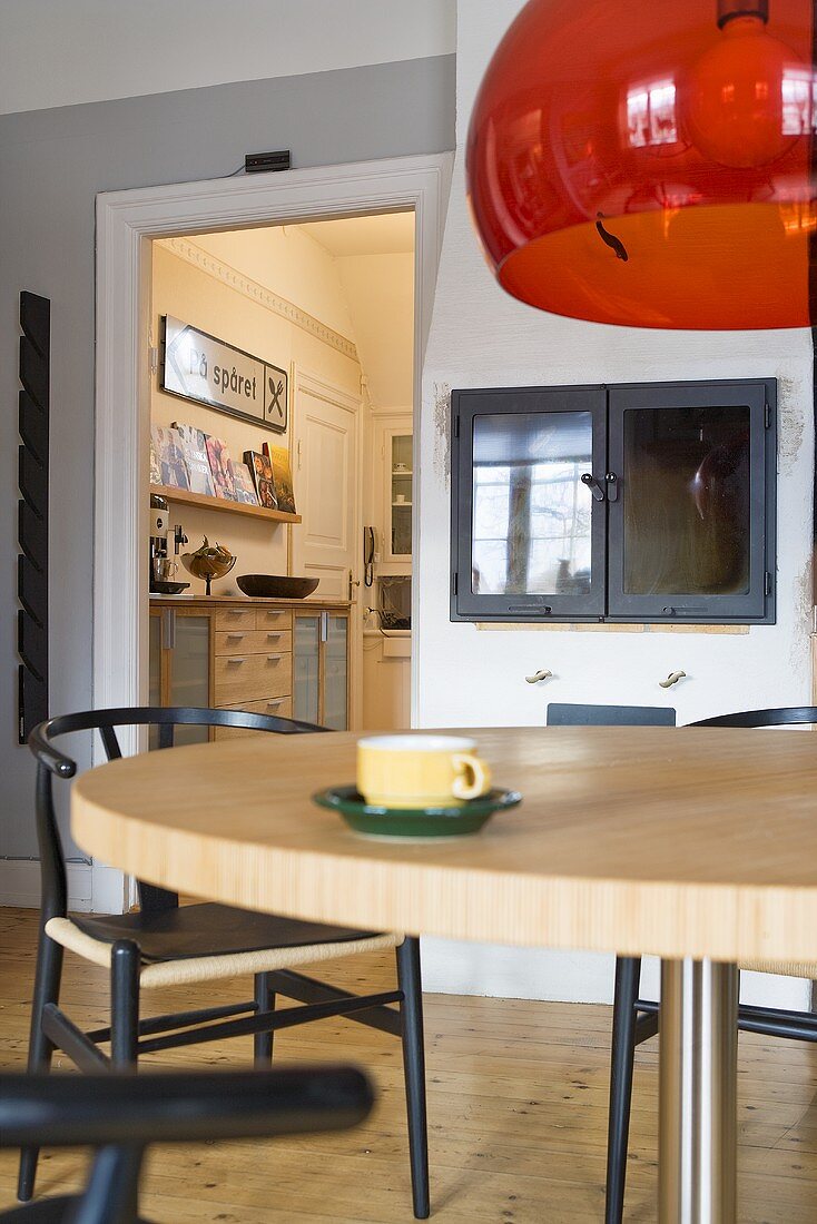 Roter Glasschirm einer Hängelampe über Essplatz und Blick durch Tür auf Küche