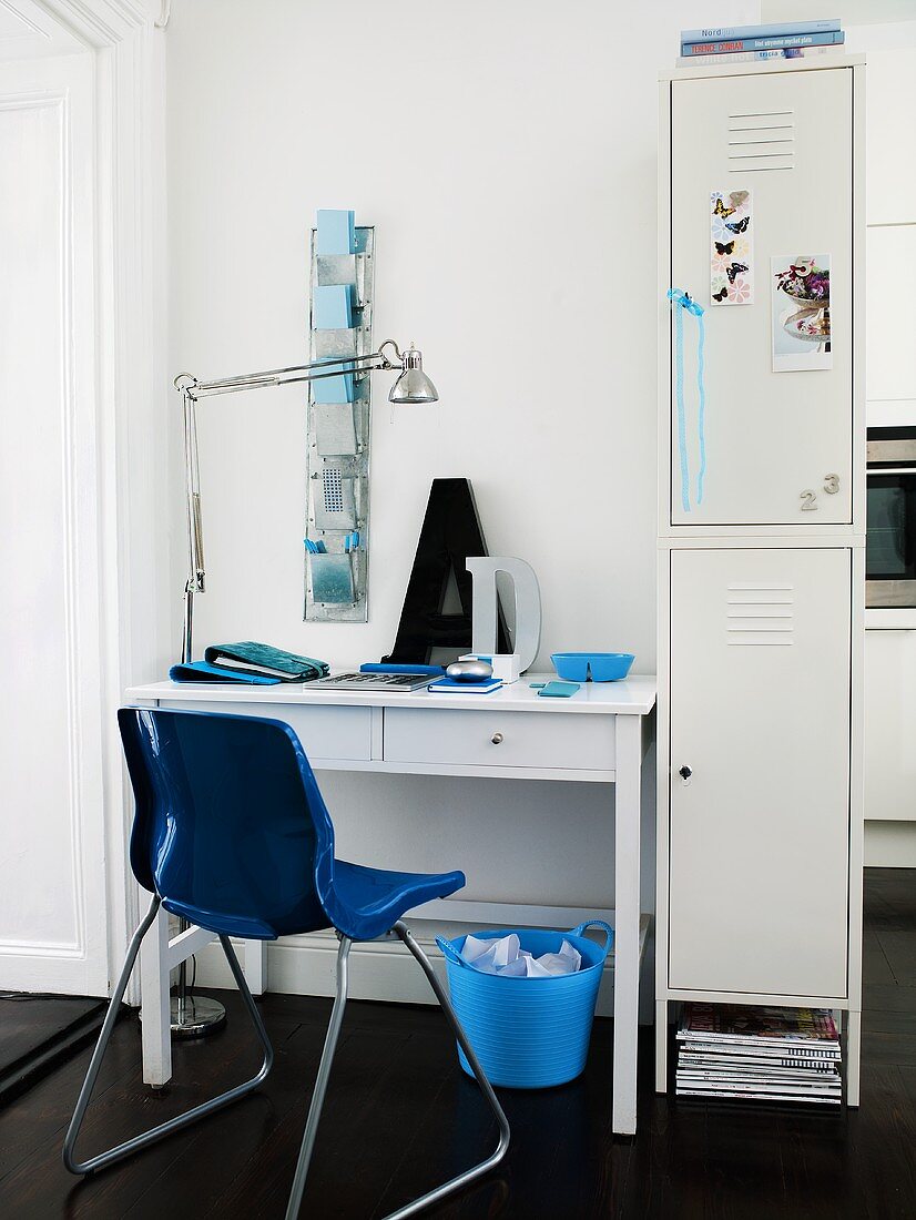 Schreibtisch und blauer Schalenstuhl aus Kunststoff neben weißem Spindschrank