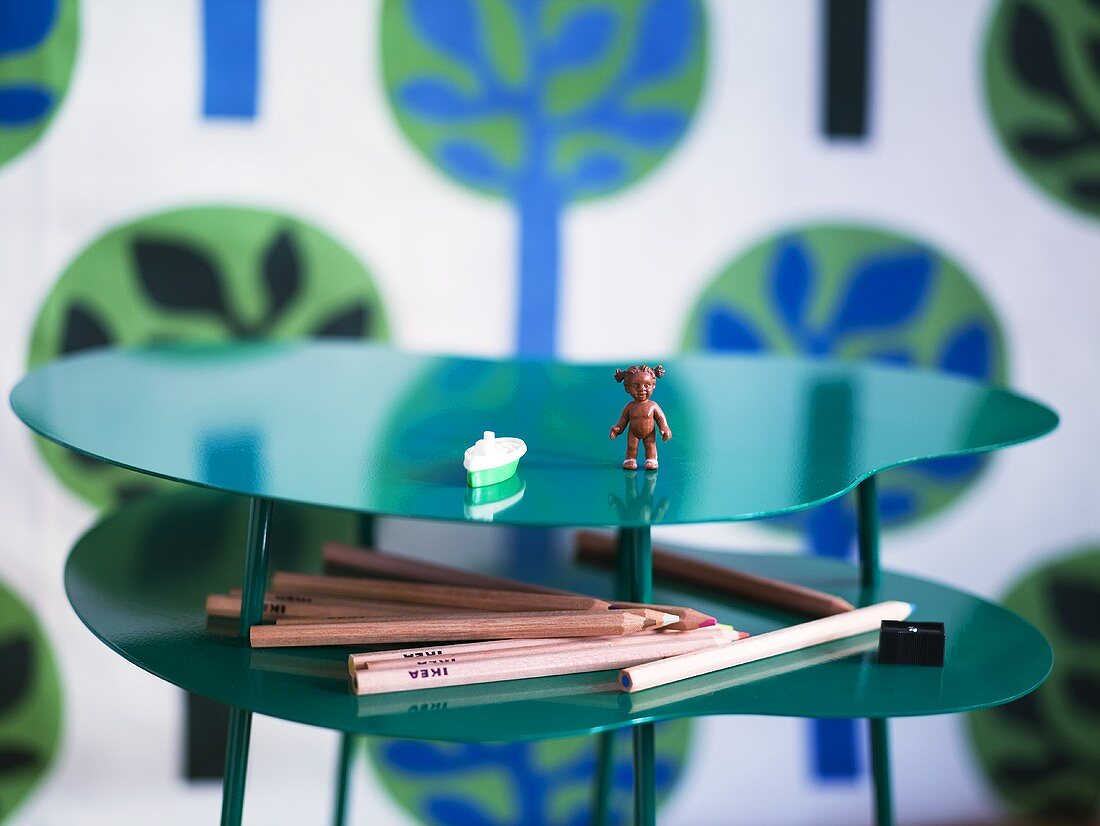 A toy figure and coloured pencils on a curved table made of shiny green metal