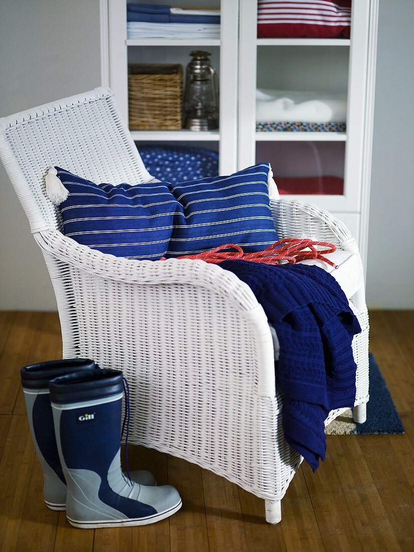 White wicker chair with blue pillows and galoshes in front of a display cabinet