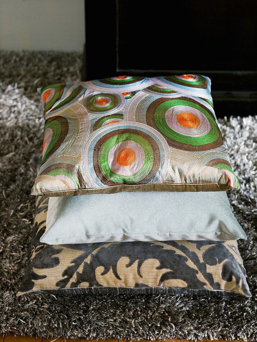 A stack of cushions with geometric and floral pattern on a flokati rug
