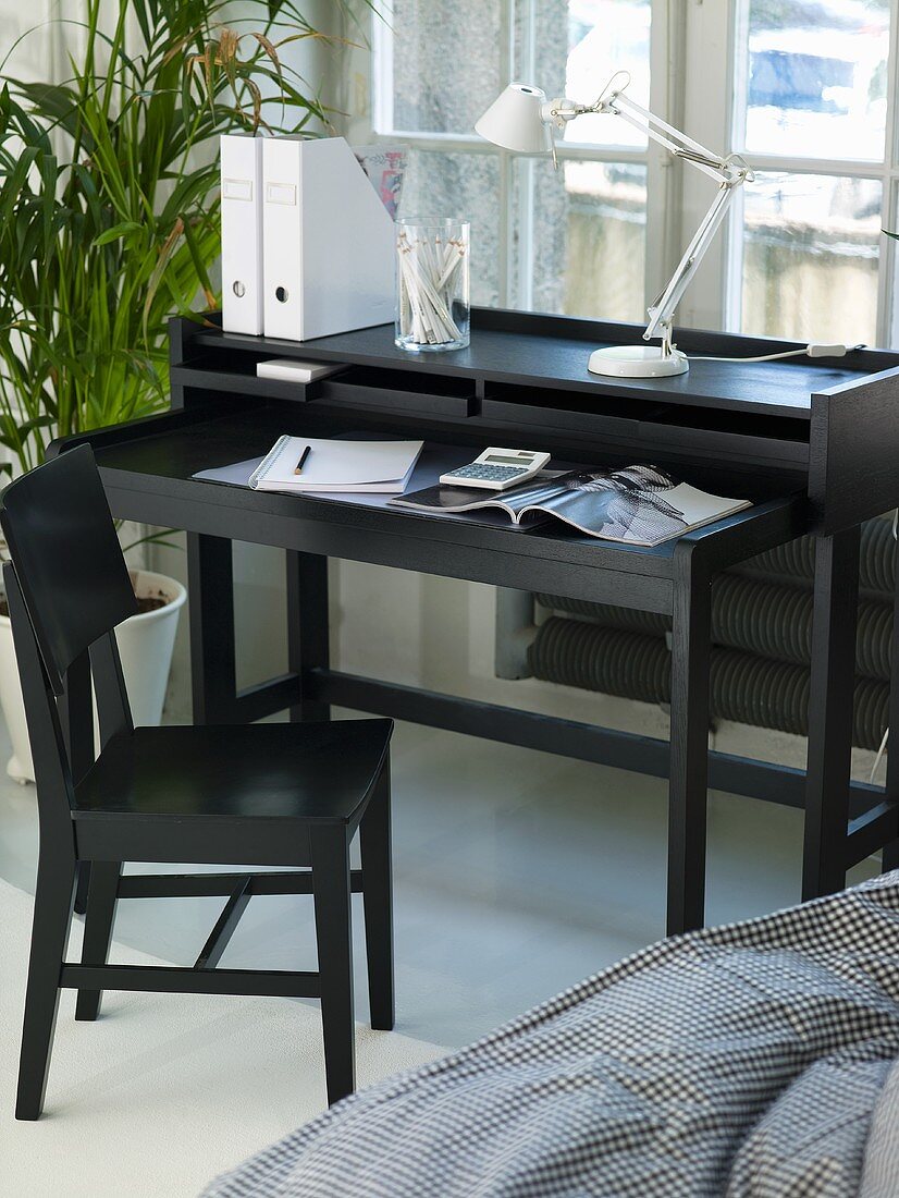 Designer Sekretär aus schwarzem Holz mit Designer Schreibtischlampe und schwarzem Holzstuhl vor Fenster