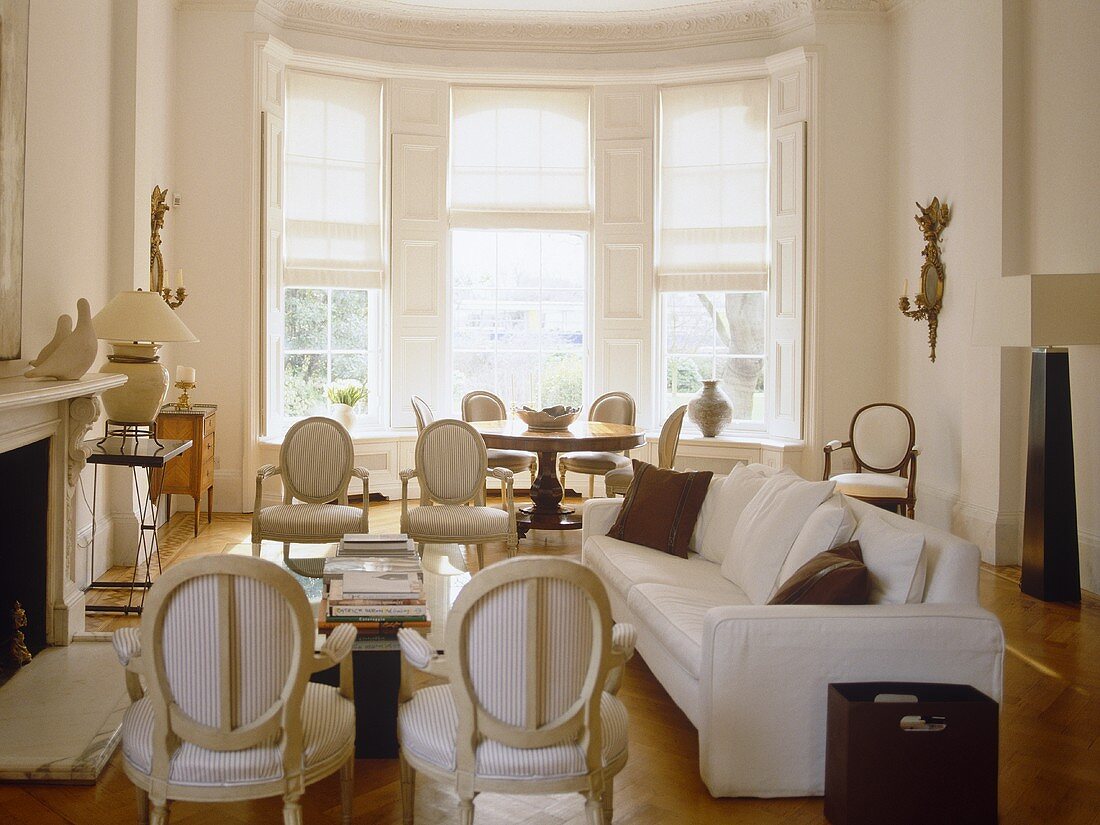 weiße Polsterstühle im Barockstil und modernes Sofa im Kaminzimmer