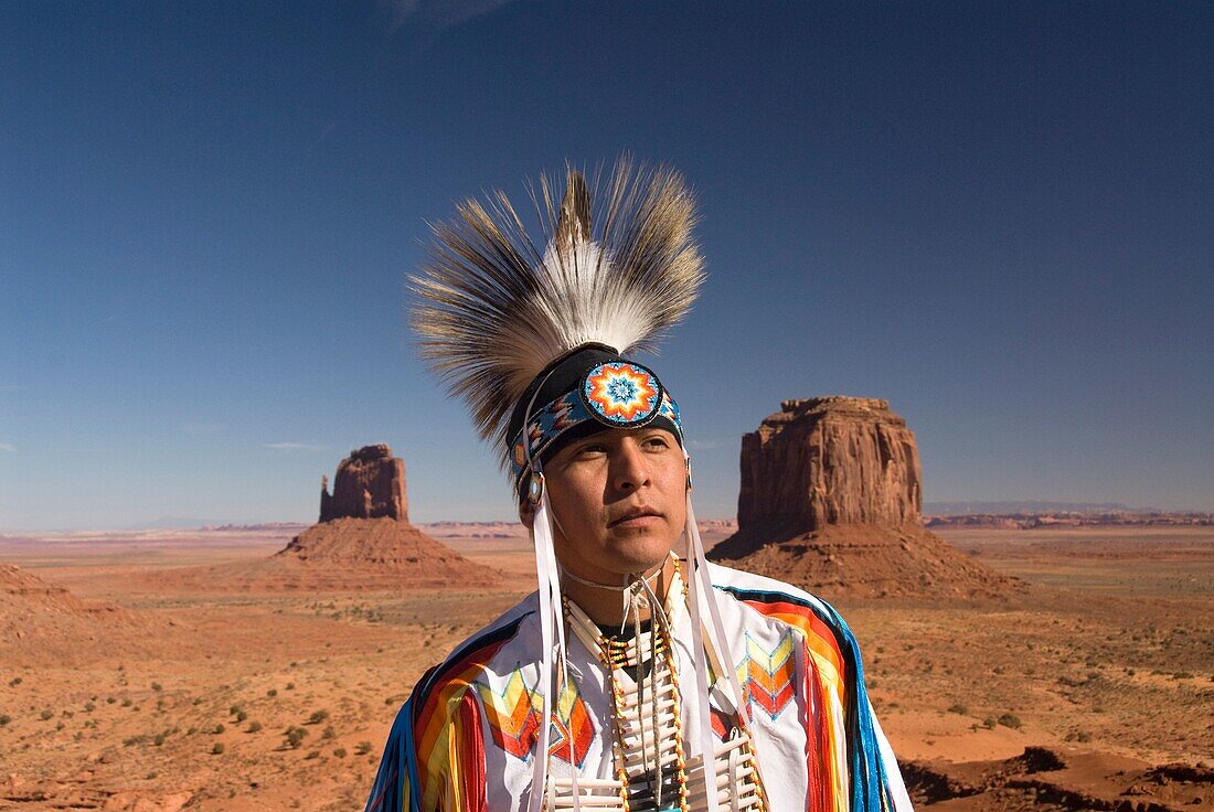 Navajo Indian dressed in a traditional costume, in background is Merrick Butte right and East Mitten Butte left, Monument Valley Navajo Tribal Park, Arizona, USA