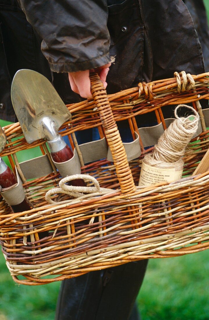 Woman carrying a wooden storage basket filled with garden tools and equipment