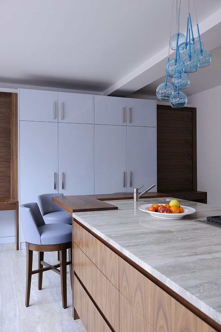 Blue bar stools at island unit breakfast bar with wooden drawers in contemporary kitchen