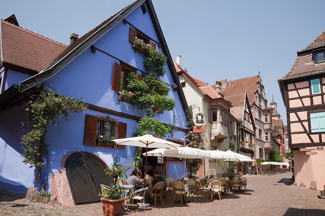 Riquewihr, Alsace, Haut-Rhin, France, Europe  A la Couronne restaurant in old building on narrow cobbled street with people dining outside in picturesque medieval town on the Alsatian wine route