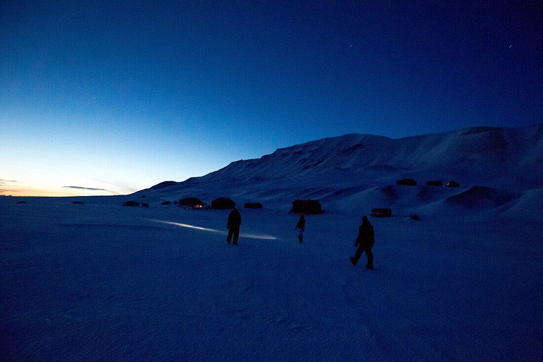 Personen gehen in der nacht durch die winterliche Landschaft von Spitzbergen, Svalbard, Norwegen