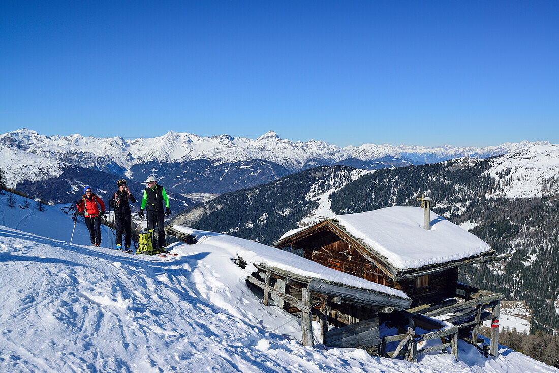 Drei Personen auf Skitour machen an Almhütte Pause, Stubaier Alpen im Hintergrund, Gammerspitze, Schmirntal, Zillertaler Alpen, Tirol, Österreich