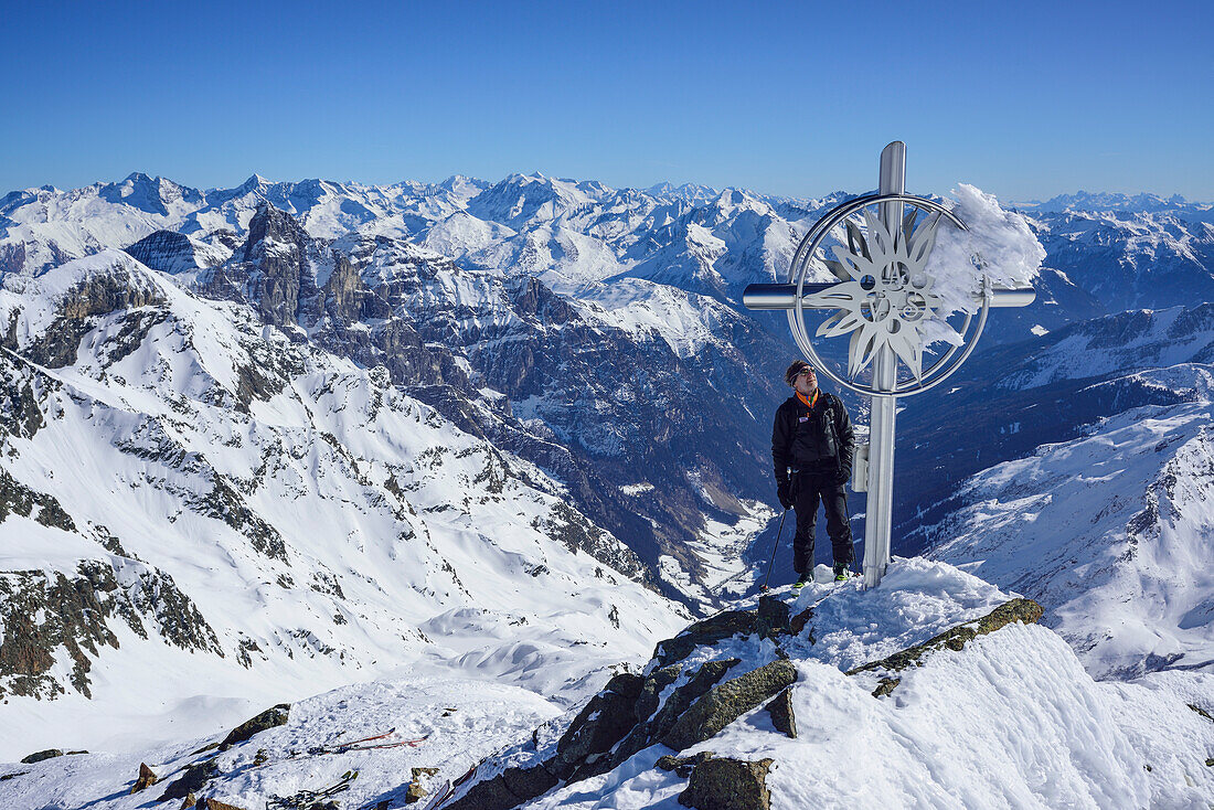 Mann auf Skitour steht am Gipfelkreuz der Schneespitze, Stubaier Alpen mit Tribulaun und Zillertaler Alpen im Hintergrund, Schneespitze, Pflerschtal, Stubaier Alpen, Südtirol, Italien
