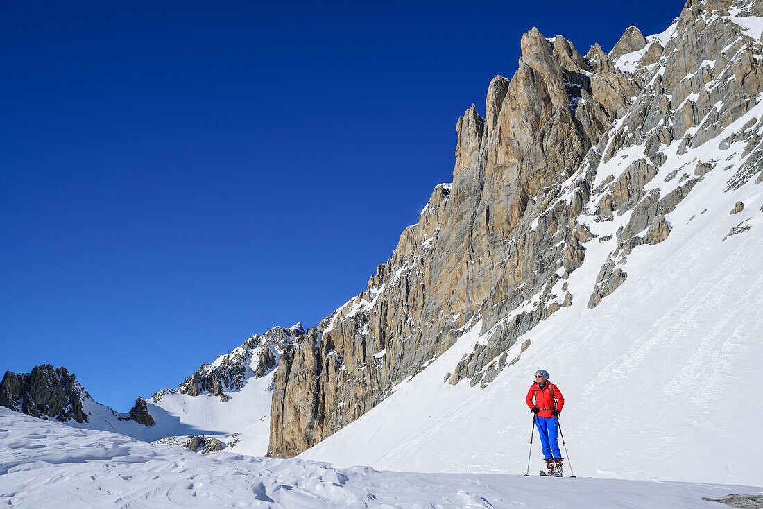 Frau auf Skitour steht unter den Felswänden des Monte Sautron, Valle Maira, Cottische Alpen, Piemont, Italien