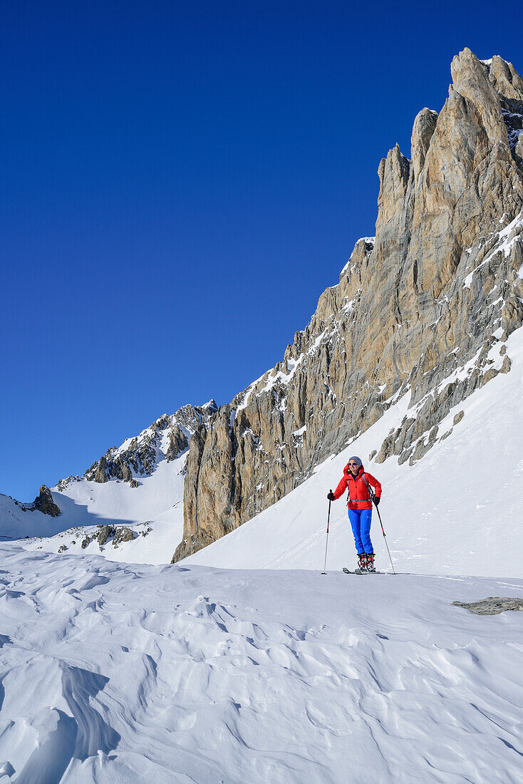 Frau auf Skitour steht unter den Felswänden des Monte Sautron, Valle Maira, Cottische Alpen, Piemont, Italien