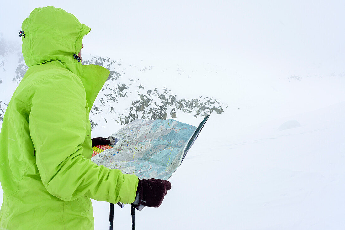 Frau auf Skitour blickt bei Schlechtwetter auf Landkarte, Serriera di Pignal, Valle Stura, Cottische Alpen, Piemont, Italien