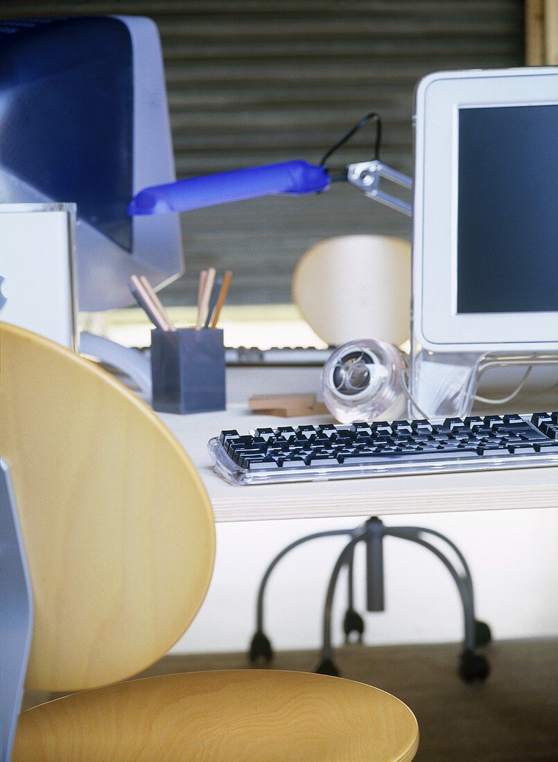 A detail of a modern home office showing a desk, computer screen, keyboard, wooden chair