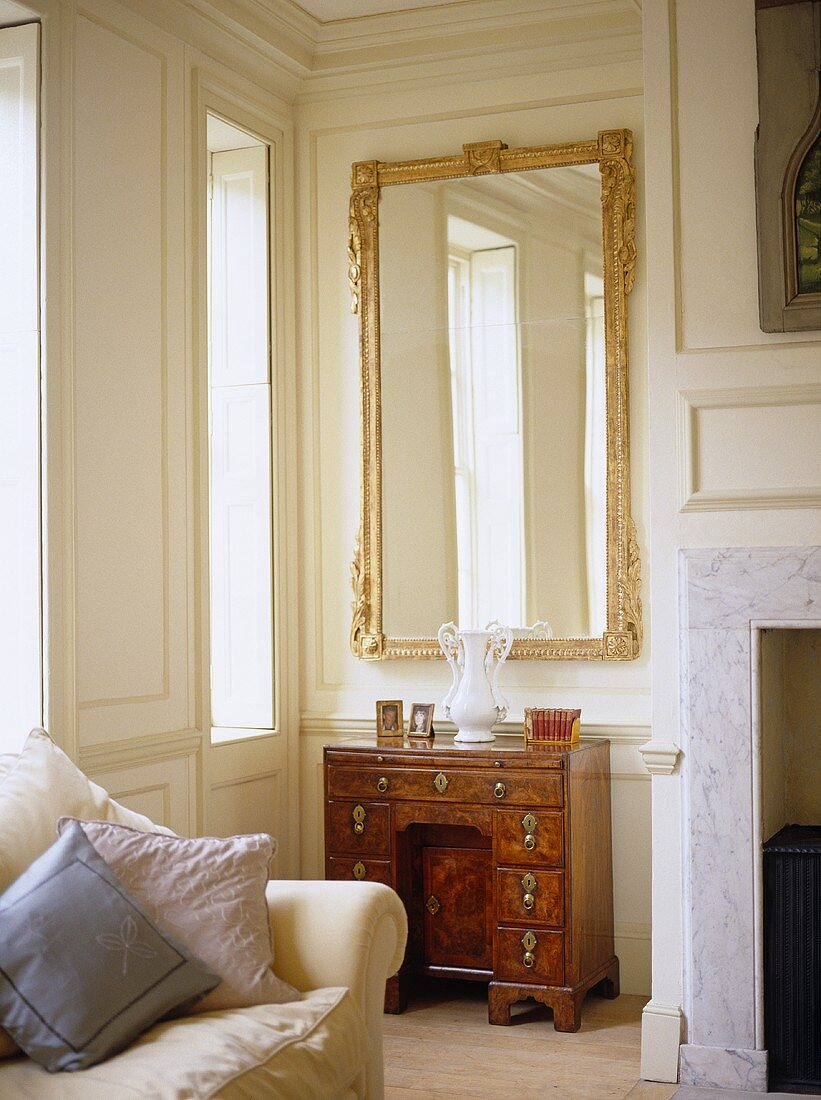 Spiegel mit Goldrahmen über antikem Schreibtisch in Wohnzimmerecke mit weisser Holzveräfelung